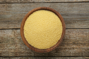 Bowl of raw couscous on wooden table, top view