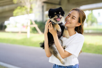 Happy young asian woman playing and sitting on road in the park with her dog. Pet lover concept