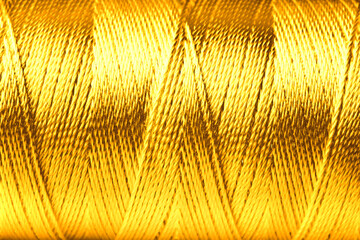 Obraz premium Spool of golden sewing thread as background, closeup