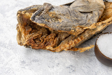 Close-up of the head of a salted cod next to a bowl with grains of sea salt