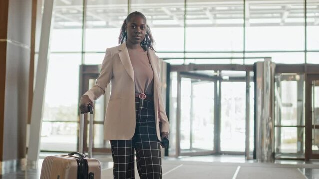 Portrait of young African American woman having business trip standing with suitcase in hotel lobby