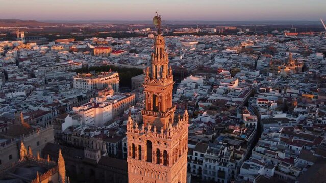 Giralda (bell tower) of Seville Cathedral lit up by sunset; sunset drone orbit