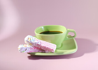 Espresso and Sweetness: A Green Mug of Black Coffee and a Pastel Pink Wafer Cookie with Icing and Sprinkles