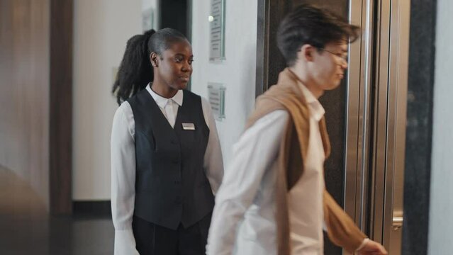 Slow motion of African American female porter or concierge offering hotel guests to get in elevator