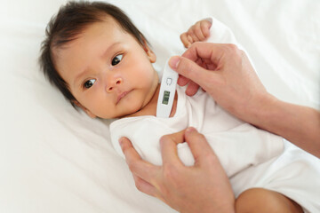 mother measuring temperature at armpit of ill baby. sick child with high fever on bed - obrazy, fototapety, plakaty