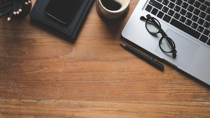Top view of laptop computer, eyeglasses, smart phone, coffee cup and notebooks on wooden desk. Top...
