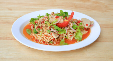 Spicy Instant Noodle Salad with Sliced Vietnamese Pork Sausage in white plate on wood background - Thai food.