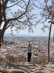a hispanic man with a hat standing with open arms in the top of a mountain travel in mexico with a hispanic city atlixco puebla in the background