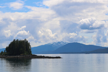 Amongst the pines and rocks of this small island in Alaska. Surrounded by the seawater and flanked by tall blue mountains.  All is tranquil as the clouds roll over the picturesque terrain 