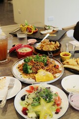 Brunch scene with several meals, drinks, salads, bread, rice, pasta and thick soup on the table