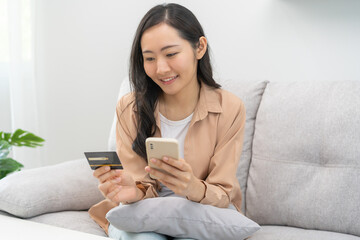 Cardboard box parcel in a trolley, asian young woman using mobile phone with shopping service on market place, website direct buy goods from seller over internet. Online shopping at home, delivery.