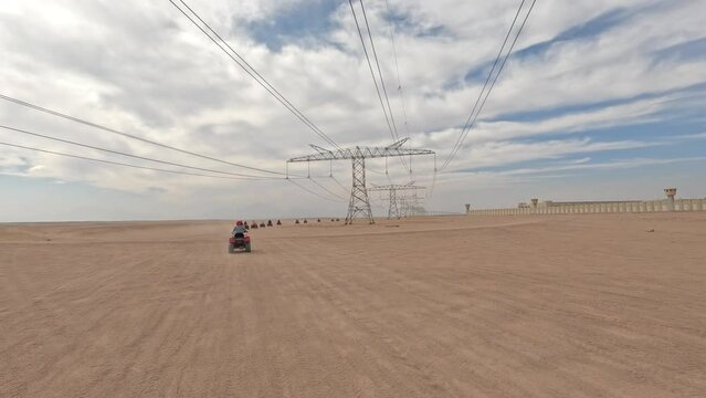 Long line of tourists on four wheelers in the Sinai Desert under a sunny sky and powerline transmission towers