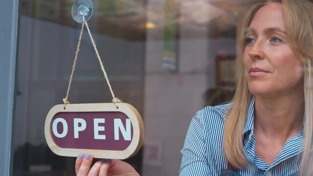 Woman working in shop or cafe turning round sign in door from closed to open - shot in slow motion