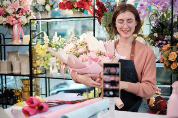 E-commerce business, one young White female florist demonstrates and shows floral arrangements via...