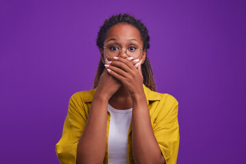 Young shocked African American woman covers mouth with hands after learning secret and tries not to...