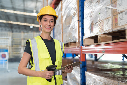 Female warehouse worker wearing hard hat and uniform checks stock, inventory with ipad tablet on shelf pallet in the storage warehouse