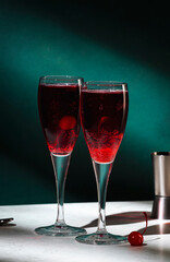 Kir Royale alcoholic cocktail with blackcurrant liqueur, prosecco and cocktail cherry. Dark green background, hard light and shadow pattern