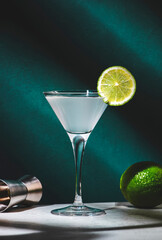Vodka gimlet alcoholic cocktail drink with vodka, syrup, lime juice and ice, dark green background, bright hard light and shadow pattern