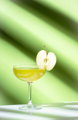 Apple pie alcoholic cocktail beverage with vodka, apple liqueur, cinnamon syrup.. Light green background, hard light, shadow pattern. Minimalistic style