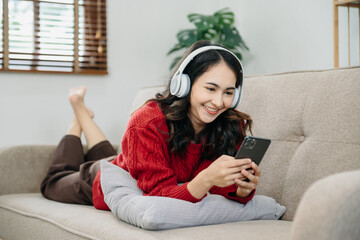 ￼Smiling girl relaxing at home, she is playing music using smartphone tablet, laptop, and wearing white headphones..