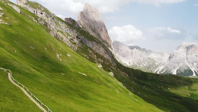 Green meadow slope and pathway leading up to Dolomites of Italy, aerial view