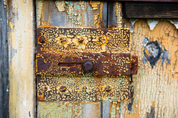 Rusty metal bolt and latch close-up on old shabby wooden door. Chunks of paint, peeling paint, corrosion of metal, Rusty metal. Decay and ruins.