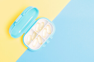 Plastic box pills with vitamins close-up on yellow and blue background top view.