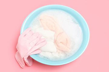 Wash basin with clothes and rubber gloves on pink background close-up, top view.
