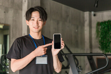スポーツジムでスマホを持つスタッフ・トレーナー・インストラクター・作業療法士・理学療法士・柔道修復士
