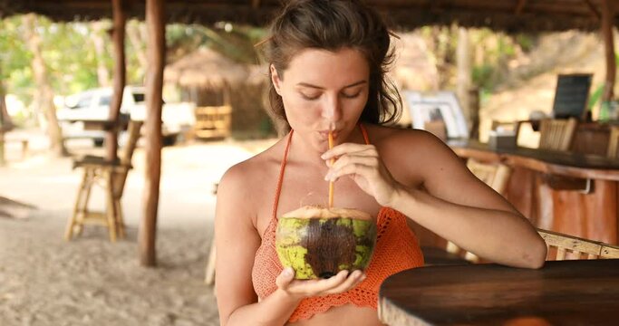 Young woman sitting in authentic beach bar with a coconut drink