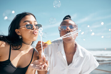 Friends, playing or blowing bubbles by beach, ocean or sea in summer holiday, travel vacation or bonding activity. Women, people or students and soap wand or toy in fun game, freedom or social break - Powered by Adobe
