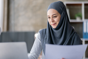 Business Asian muslim woman using calculator and writing make note with calculate doing math finance on an office desk. Woman working at office with laptop and tax, accounting, documents on desk