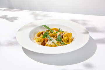 Italian ravioli with meat and mushroom sauce on white plate. Meat tortellini with creamy sauce in summer menu with shadows of tree leaves Ravioli stuffed beef in elegant style