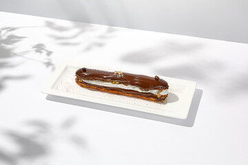 Chocolate eclair on white plate. French dessert stuffed custard cream. Eclair with coffee flavours Chocolate dessert on restaurant plate. Cchocolate eclair on light background
