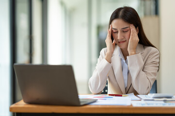 Beautiful asian businesswoman headache and stressed working in finance, management, marketing from laptop computer displaying revenue data on real estate projects in office interior.