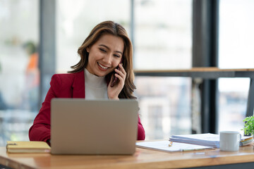 Beautiful asian businesswoman working with laptop computer is using mobile phone for talking. Finance business contacts in real estate projects in her office.