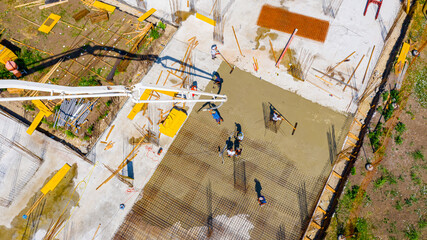 Above top view rigger, worker is holding pump hose to pouring fresh concrete into building foundation over reinforcing steel bars