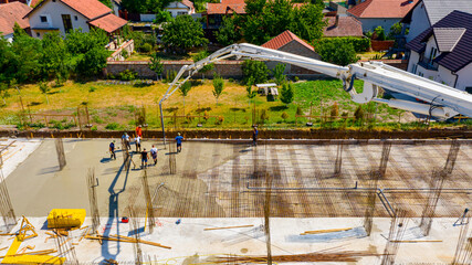 Above view rigger, worker is holding pump hose to pouring fresh concrete into building foundation over reinforcing steel bars