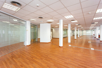Large empty space with ceiling tiles, fluorescent lights, light brown laminate flooring and white...