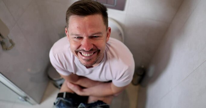 Portrait of smiling man sitting on toilet with joyful emotions on face