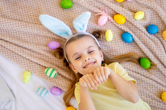 easter, a little child girl among painted colored eggs is preparing for the holiday smiling and having fun, top view