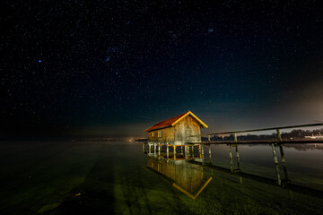 kleines Bootshaus in Stegen am Ammersee unter Sternenhimmel mit Spiegelung