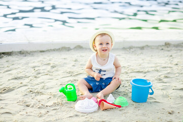 a baby boy of six months plays in the sand with toys on the embankment by the water of the sea, the concept of recreation and travel