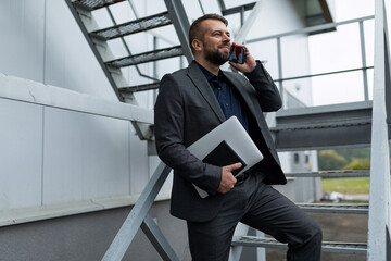 Caucasian business man in formal suit with laptop talking on the phone outside