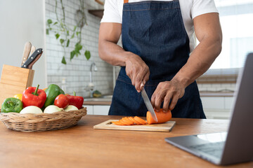 Asian strong man Wearing an apron having fun while preparing ingredients such as fruits and vegetables. learn how to do Chopping Carrots via Application Happily online in the kitchen.