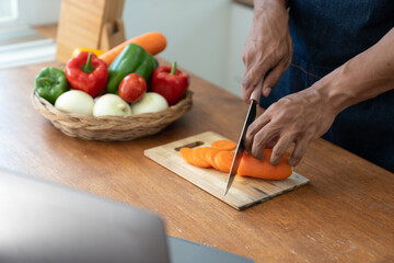 Asian strong man Wearing an apron having fun while preparing ingredients such as fruits and vegetables. learn how to do Chopping Carrots via Application Happily online in the kitchen.