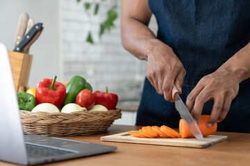 Asian strong man Wearing an apron having fun while preparing ingredients such as fruits and vegetables. learn how to do Chopping Carrots via Application Happily online in the kitchen.