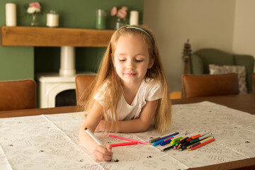 The girl paints an Easter picture lying on the table in a bright interior