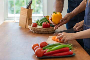 Young Asian couple wearing apron cooking healthy salad in the kitchen together picking out ingredients for the online cooking class. lifestyle and cooking concept.