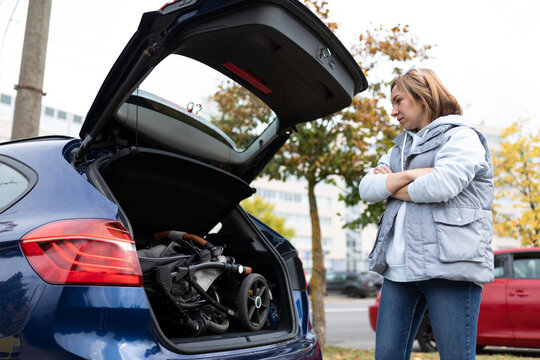 Woman At The Open Trunk Of A Car With A Baby Stroller Inside